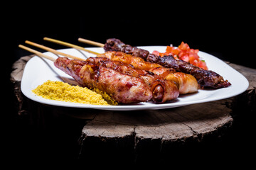 Wall Mural - Delicious barbeque and kebab served on a white plate on a wooden texture on a black background