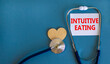 Intuitive eating symbol. White card with words Intuitive eating, beautiful blue background, wooden heart and stethoscope. Medical and intuitive eating concept.