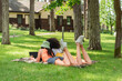 © LIGHTFIELD STUDIOS - Back view of multiethnic lesbian couple using laptop near coffee on blanket in park.