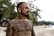 © Cavan Images - Thai guy on the seashore among the palm trees all in tattoos