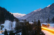 Wieczorny, zimowy krajobraz górski . W dole wioska alpejska. Żółta smuga świateł samochodów. Długi czas naświetlania.