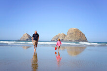 Happy Little Redhead Girl Walking Along The Ocean Shore With Grandpa.