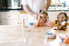 A Little Girl Getting Her Hair Done By Her Father At The Kitchen Table