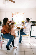 Two Parents Styling Their Twin Girls Hair Together In The Kitchen