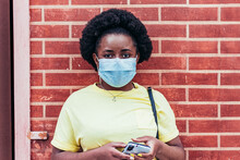Portrait Of Black African American Girl With Face Mask On Red Brick Wall Background.