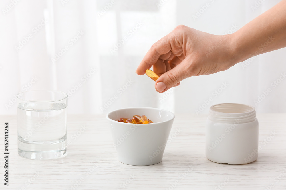 Woman taking fish oil pill from bowl on table, closeup