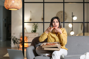 Surprised young woman eating tasty pizza at home in evening