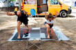 © Cavan Images - Smiling couple practice yoga on mats at camping watching video tutorial on laptop, excited man and woman repeat trainer online instructions on computer