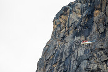 Helicopter Flies Next To Mountain Cliff.
