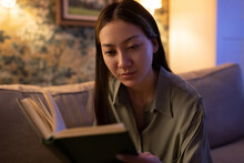 Focused Asian Woman Reading Book In Evening