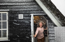 Woman Holding Door Open With Hair Blowing In Snow Storm In Denmark