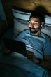 © Cavan Images - Man lying on bed with tablet in darkness
