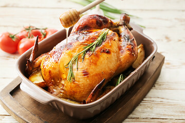 Pouring honey into baking dish with tasty chicken on light wooden table, closeup