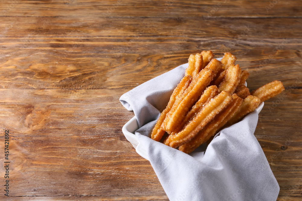 Bowl with tasty churros on wooden background