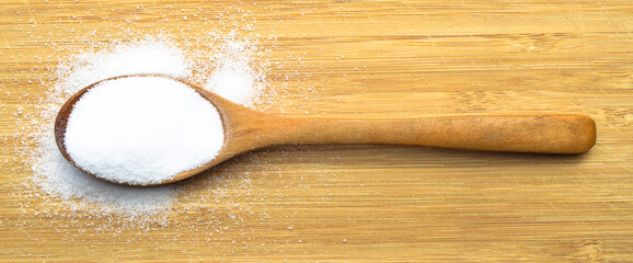 Wall Mural - Table salt used in dishes in a wooden spoon on a bamboo background