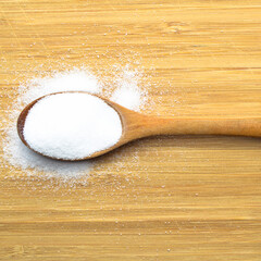 Wall Mural - Table salt used in dishes in a wooden spoon on a bamboo background