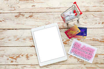 Poster - Tablet computer, shopping cart and credit cards on wooden background. Black Friday sale