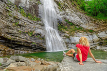 Woman Sitting By The Water Of Great Waterfall Of Bignasco, Valle Maggia, Intersection Point Between The Bavona Valley And Lavizzara Valley, Cevio In Switzerland.