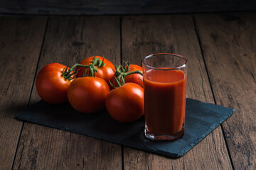 Wall Mural - Tomato juice in a glass and a fresh tomato next to it on a wooden table