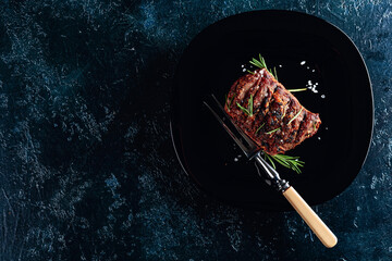 Grilled ribeye beef steak with rosemary and salt on a black plate.