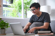 © Prathankarnpap - Young Asian man sitting on comfortable sofa and using computer laptop.