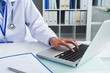 © DragonImages - Close-up image of general practitioner working on laptop and signing documents at her office desk