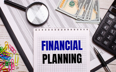 On the office table there is a notebook with the text FINANCIAL PLANNING, a pen, a calculator, dollars, multi-colored paper clips and a magnifying glass. Stylish workplace. Business concept