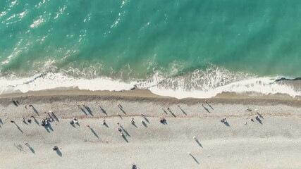 Poster - Aerial view of the sea coast. People walk along the beach and azure waves roll onto the shore. Top-down drone footage