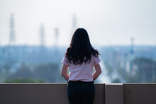 Asian Female Teen Stands Backside In Front Of City View At Rooftop Of The Building