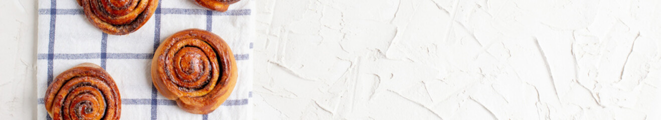 Wall Mural - banner of baked cinnamon buns on light background with checkered napkin