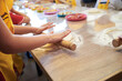 © Natalia - Child wearing yellow apron, making dough on the table. Close-up picture of hands, stretching dough with rolling pin. Bakery master class for small children. Pizza workshop at juniors' party.