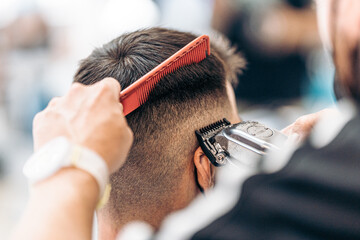 Barber cutting the hair of an adult male with a shaving machine and ca comb