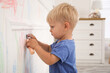 Mischievous little boy drawing with colorful chalk on white wall at home
