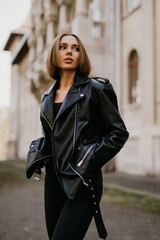 Wall Mural - Young girl in leather jacket and jeans resting outdoors. portrait of woman in the city