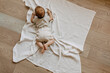 Baby lying on tummy on a white muslin blanket on the floor, top view.