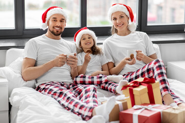 Poster - family, winter holidays and people concept - happy mother, father and little daughter with christmas gifts drinking coffee and eating coookies in bed at home