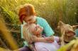 © sergiymolchenko - Lesbian young woman with haircut hugs pretty girlfriend sitting with funny red dog in green field grass at sunset in summer evening