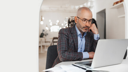 Businessman working on laptop in a cafe and ponders, free space for insertion