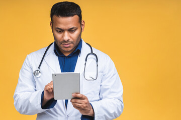 Portrait of african american black indian doctor man using a tablet computer isolated over yellow background.