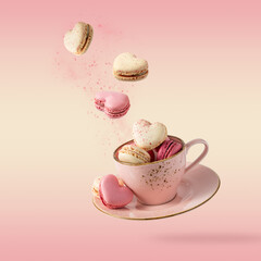 Wall Mural - French sweet colorful cookies macarons macaroons in vintage pink cup flying isolated  on gradient yellow pink background.