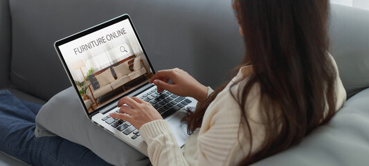 Young Asian woman in casual clothes using laptop computer relax sitting on couch sofa at home. Asian surfing the internet looking for the furniture Online. Furniture Online shop website e-commerce.