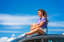 A Young Woman In Shorts Is Sitting On The Roof Of A Volkswagen Tiguan Car With A View Of A Beautiful Blue Sky With Clouds. The Concept Of Traveling By Car. Sudak, Crimea - 2 Sep 2021