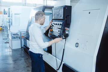 Young male engineer operating CNC machinery in iron metal factory