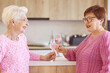 © k8most - two stylish senior women in pink sweaters drinking rose wine at modern kitchen gossiping. Friendship, talk, gossip, event, relationships, news, family concept