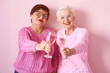 © k8most - two stylish senior women in pink sweaters with rose wine glasses on pink background. Friendship, talk, gossip, relationships, news, family concept