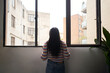 © CarlosBarquero - Rear view African girl leaning out of the window, looking outside where there are large buildings.