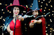 © Bangkok Click Studio - Shiny glossy paper confetti popper cracker exploded when pulled by two happy funny excited female models in black red witch dress costume tall hat and shawl in blurred background in Halloween party