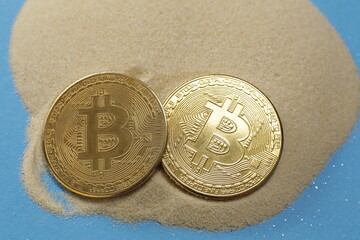 Two bitcoin coins on the sand on a blue background