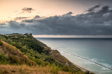 Wall Mural - Beautiful view of a hill covered with bushes and grass by the sea under a cloudy sky