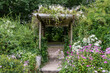 Flowers drape over and surround an old wooden pergola in the garden.